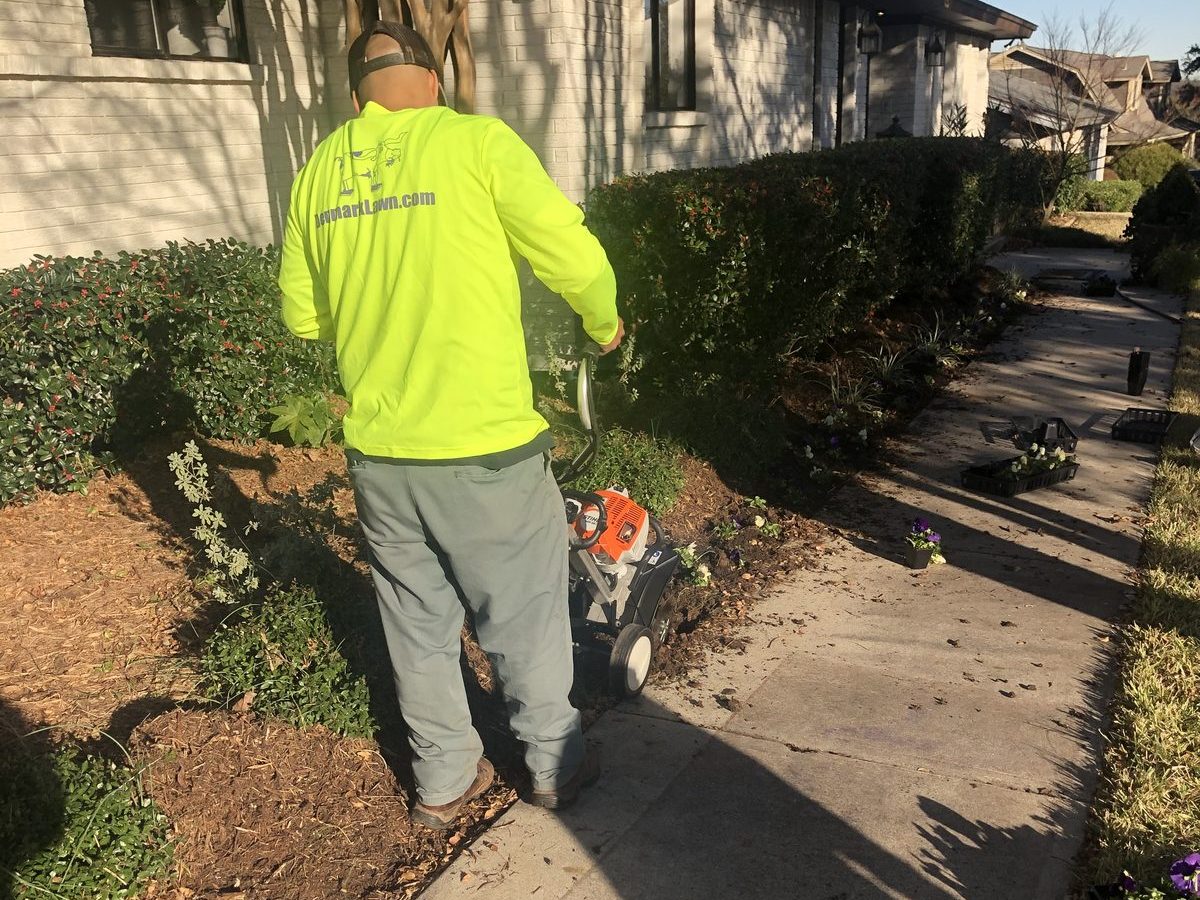 Denmark Lawn crew member edging a shrub bed and planting seasonal pansies