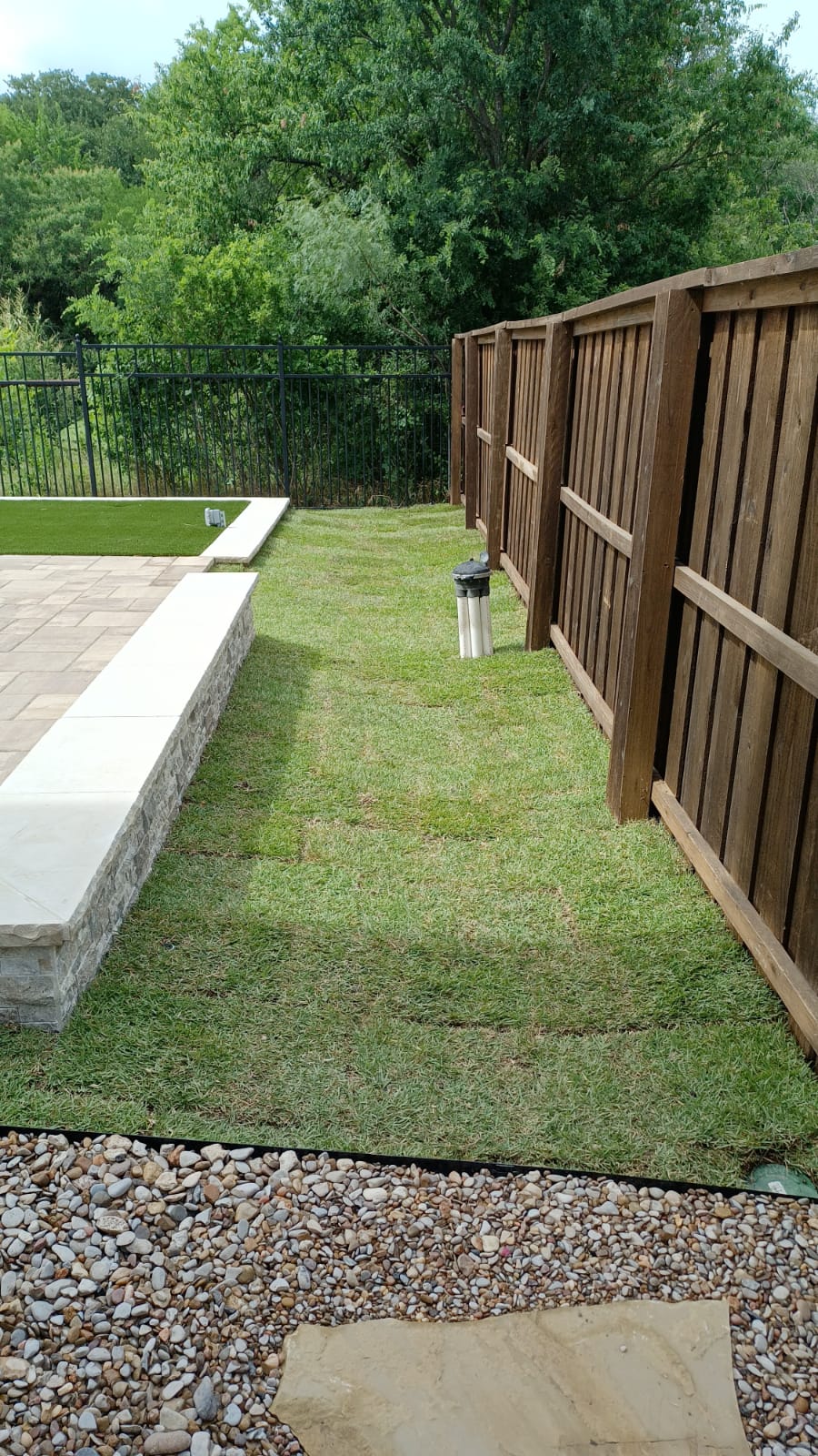 New sod along a west Fort Worth patio, fence, and river-rock bed